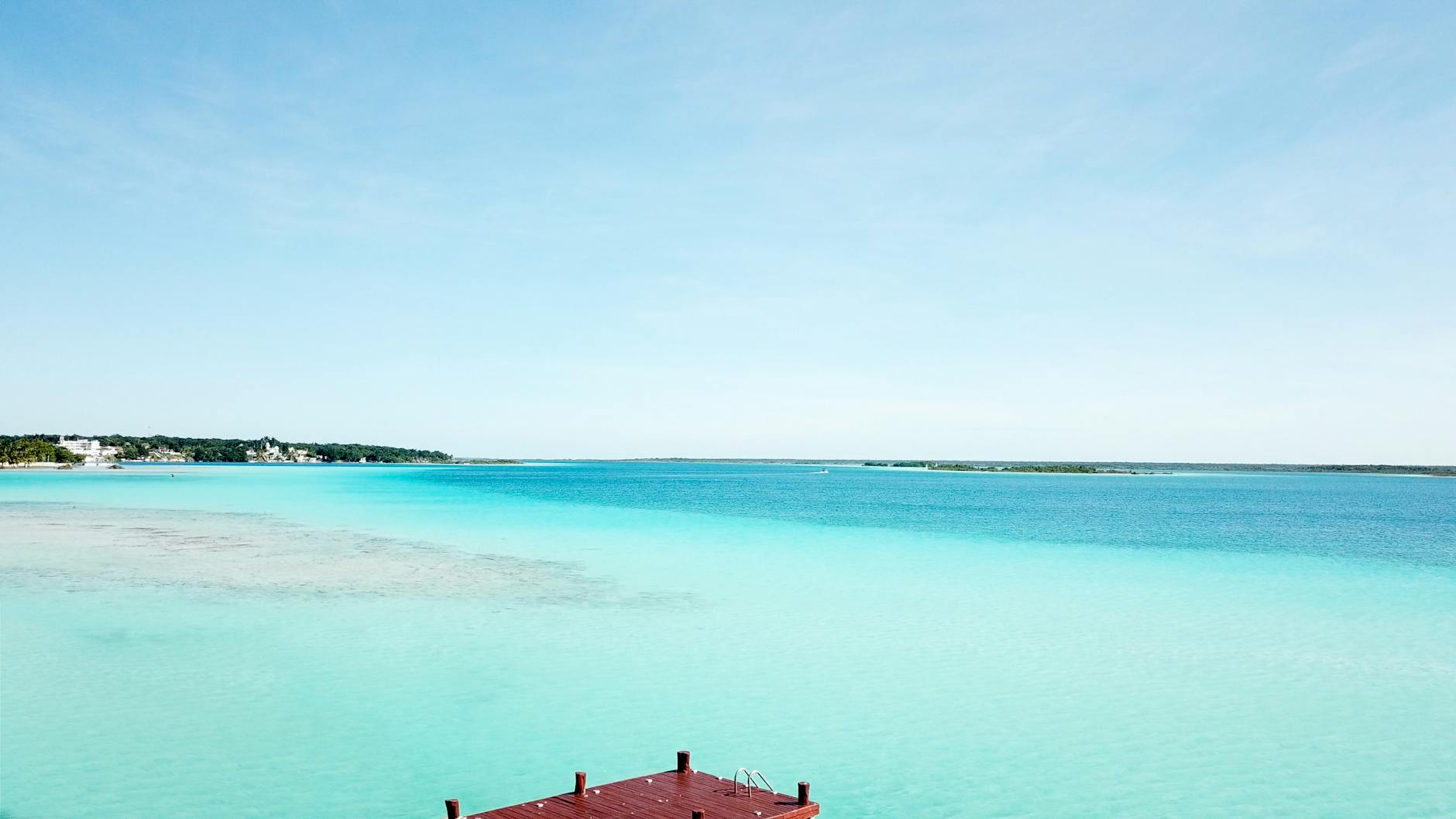 Muelle de madera en Bacalar con el reflejo del amanecer sobre la laguna turquesa